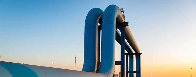 Large industrial pipeline extending toward an energy facility and port infrastructure at sunset.