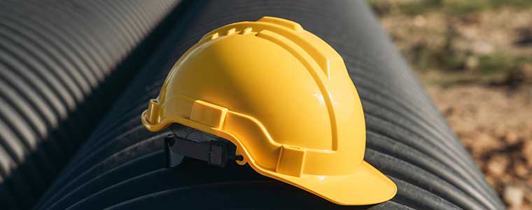 Yellow hard hat resting on a large industrial pipeline in an outdoor setting.
